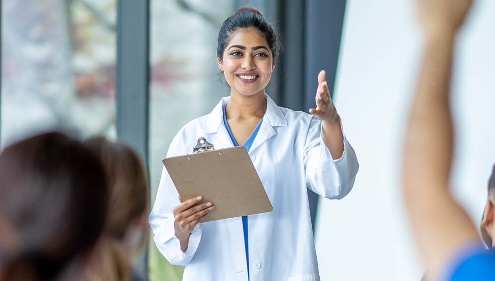 health educator in doctors coat standing in front of classroom