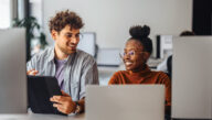 Smiling co-workers seated before a row of computer and tablet screens