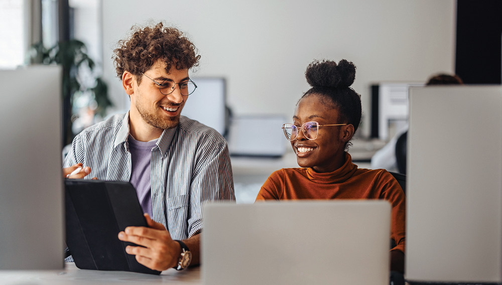 Smiling co-workers seated before a row of computer and tablet screens