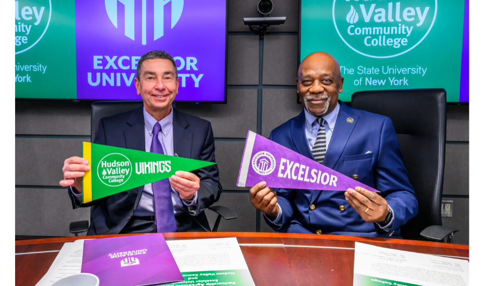 Excelsior University President David Schejbal and Hudson Valley Community College Officer in Charge Louis Coplin pose with college pennants to celebrate the institutions' expanded partnership agreement.