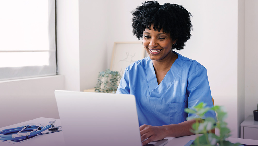 A smiling nurse informaticist works at a laptop.